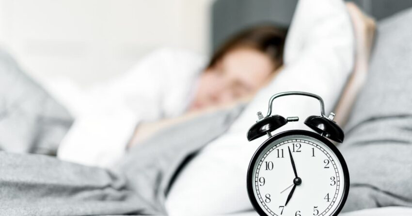 An alarm clock on a blurred background of someone sleeping, depicting their morning routine.