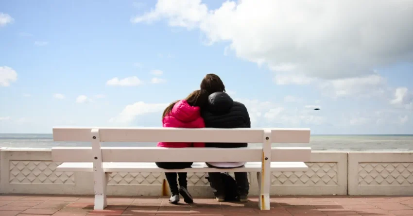 An image of a couple sitting on a bench, and facing the ocean- highlighting the blog theme of modern dating guide.