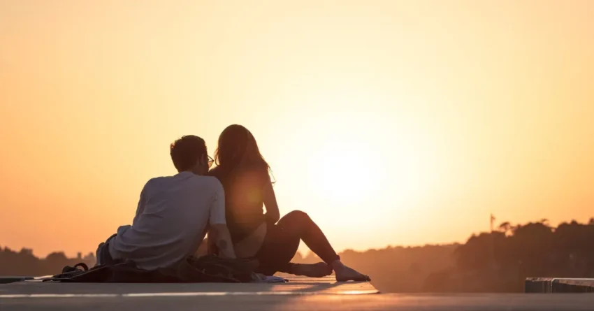 A couple staring at a sunset while sitting on a roadside, highlighting spending time together as one of the green flags in a relationship.
